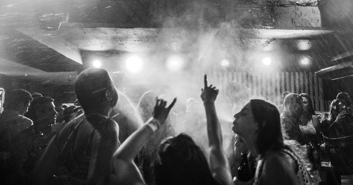 Energetic dance floor with crowd hands raised under dramatic stage lighting